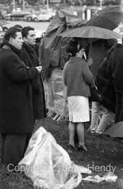 Spectators huddled under an umbrella
